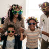 Family wearing handmade flower crowns and colorful oversized sunglasses at a Nanosarte Be the Canvas workshop