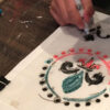 Hands drawing a heritage mandala pattern on fabric at a Nanosarte Wear Your Roots workshop