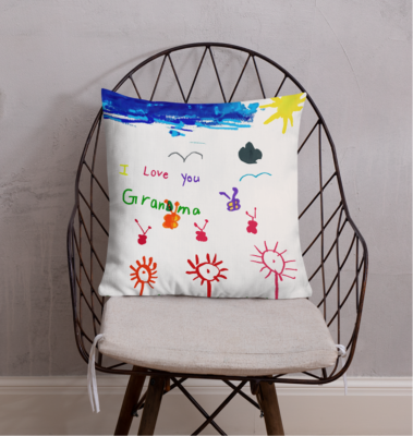 A cushion on a wire chair, printed with a child's drawing of flowers and a sun that reads "Love You Grandma"