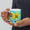 A grandmother holds a ceramic mug printed with a child's drawing of a sun, with a scannable code on the side