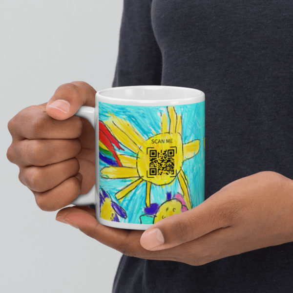 A grandmother holds a ceramic mug printed with a child's drawing of a sun, with a scannable code on the side